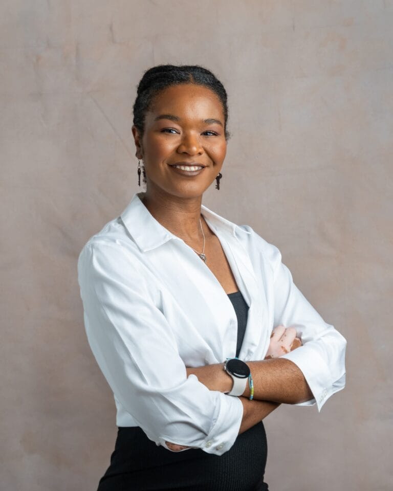 Ayanna smiling and crossing her arms in a white blouse with a black skirt.
